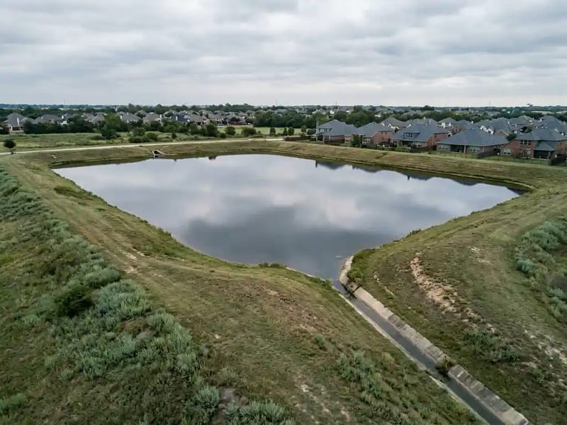 Retentiebekken met kalm water en grazige dijken in een Nederlandse woonwijk onder bewolkte lucht.
